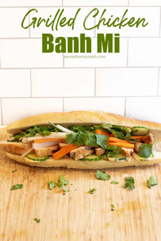 a chicken banh mi sandwich with cucumbers and carrots and cilantro on a cutting board with Pinterest pin text.