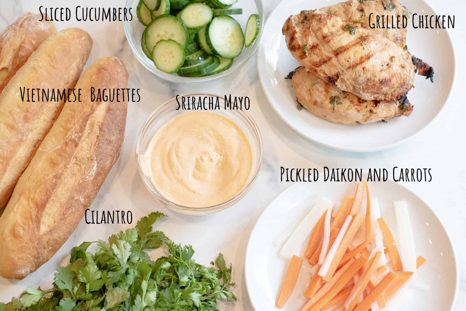 baguettes, sliced cucumbers, grilled chicken, a bowl of mayo, carrots and daikons, and cilantro labeled.