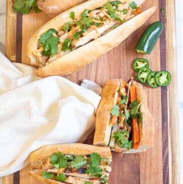 overhead of a halved banh mi and a whole banh mi on a cutting board.