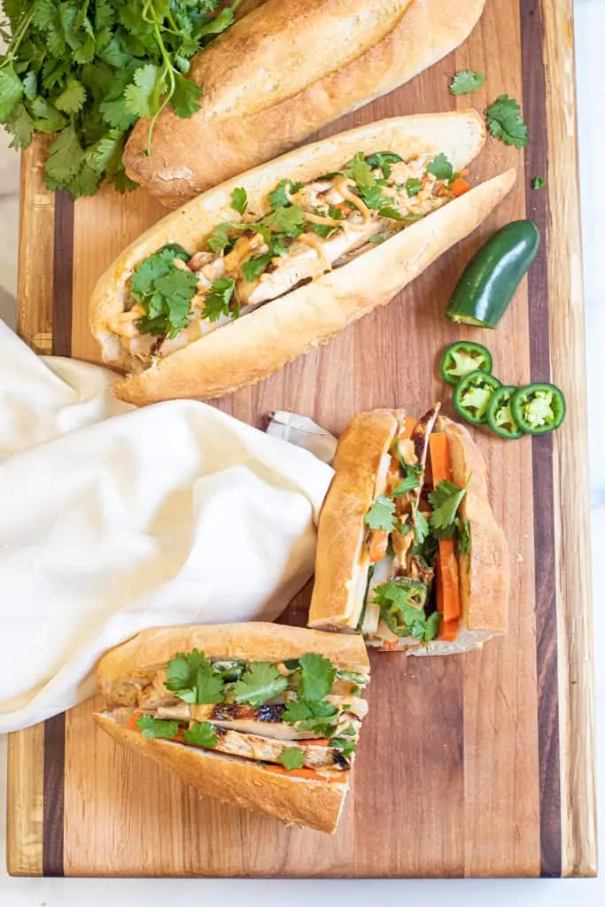 overhead of a halved banh mi and a whole banh mi on a cutting board.