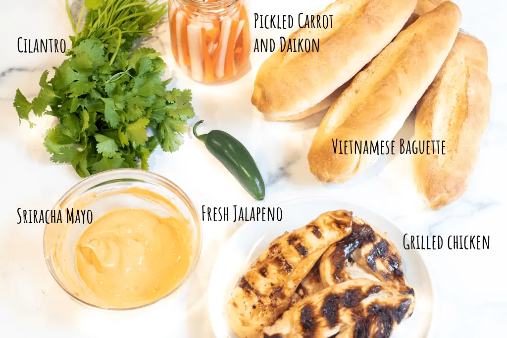 cilantro, jalapeno, grilled chicken, baguettes, jar of pickled veggies, and bowl of sriracha mayo.