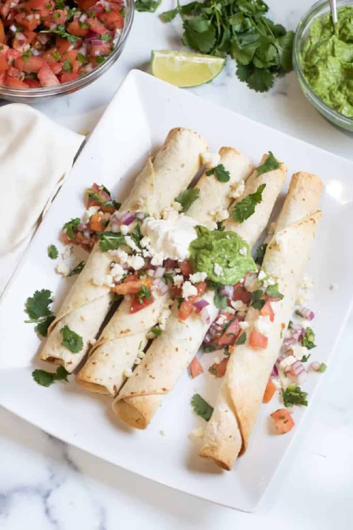 a plate of flautas topped with sour cream, gucamole, pico, and cotija cheese.