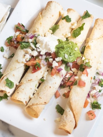 baked flautas on a plate topped with pico, guac, and sour cream.