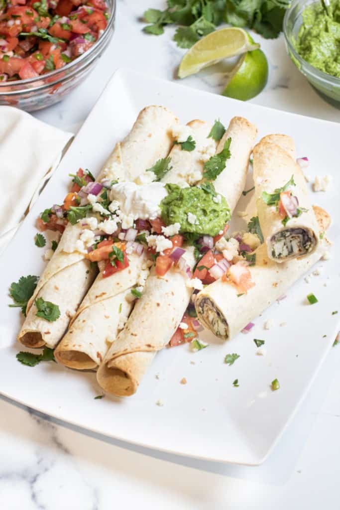 a plate of flautas topped with sour cream, gucamole, pico, and cotija cheese.
