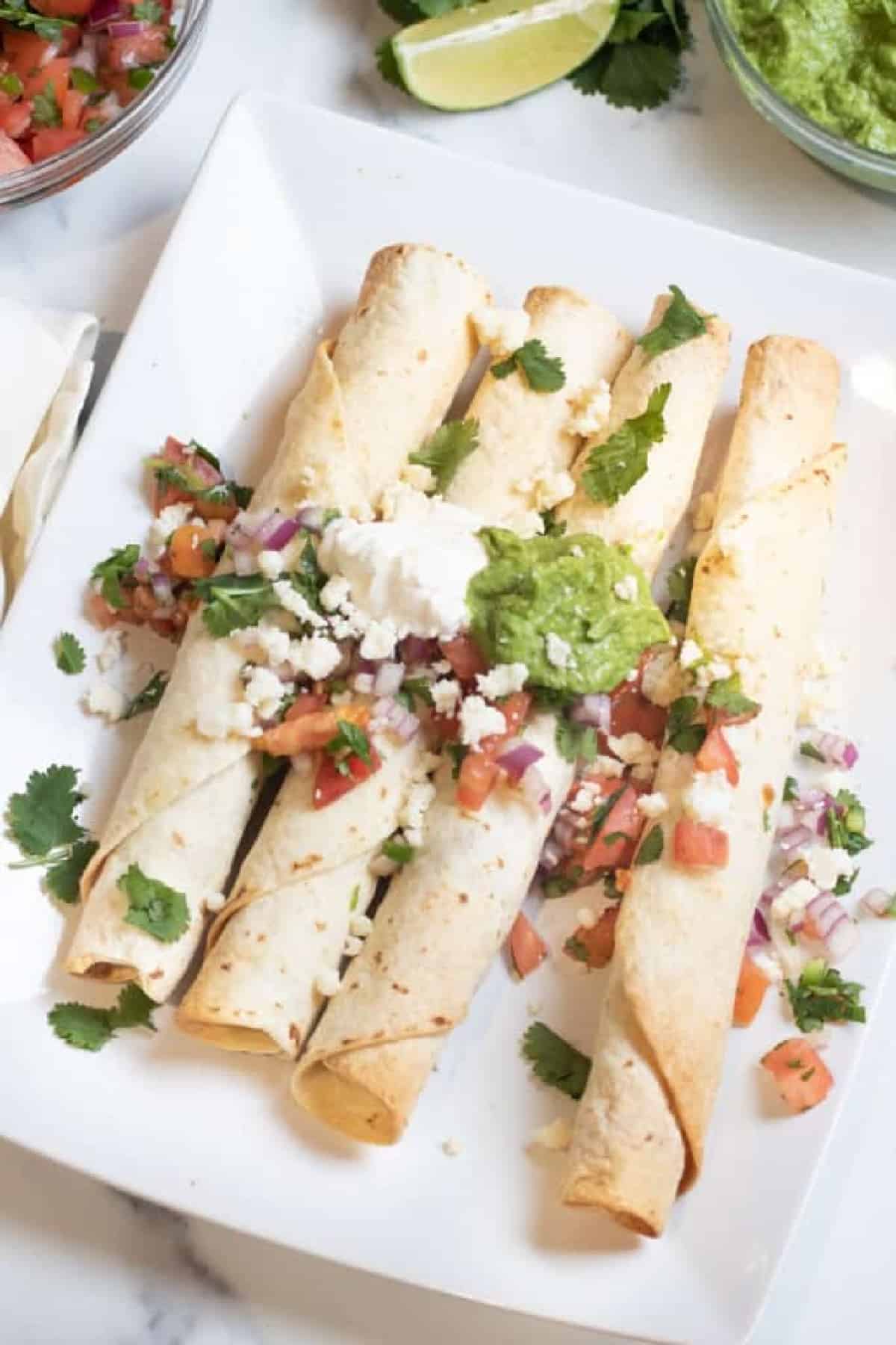 a plate of flautas topped with sour cream, gucamole, pico, and cotija cheese.