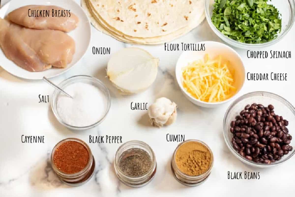 a plate of chicken, tortillas, spinach, beans, cheese, spices, onion and garlic.