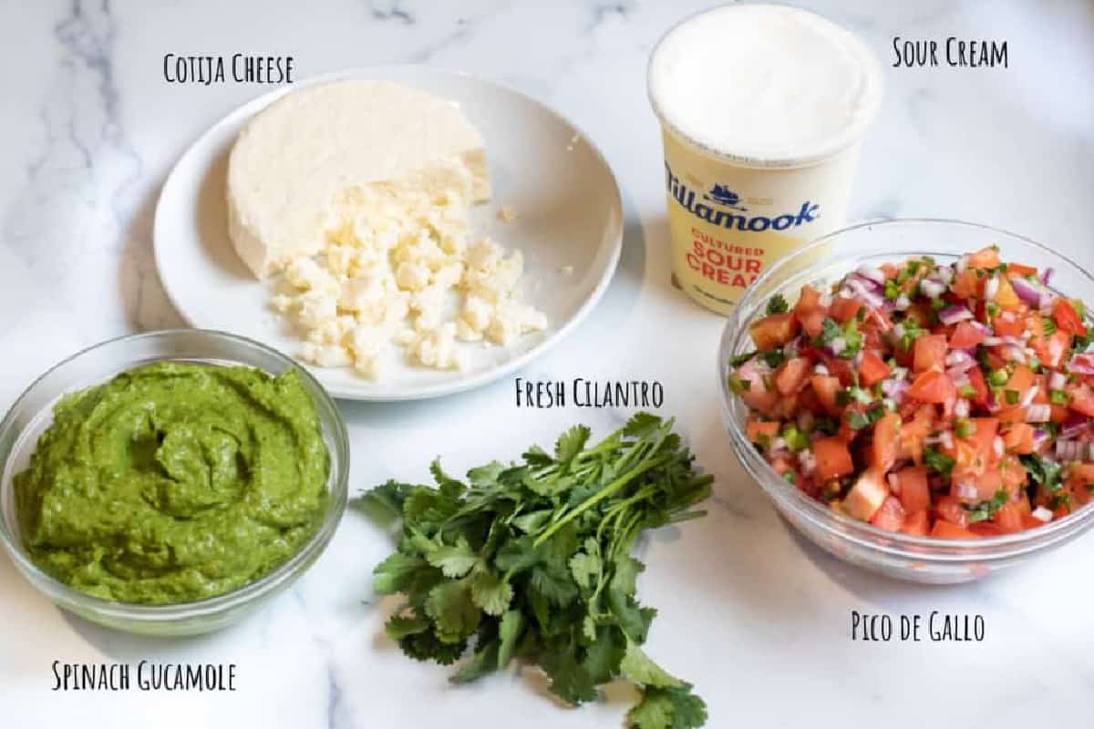 cotija, pico, guacamole, cilantro, and sour cream on a counter.