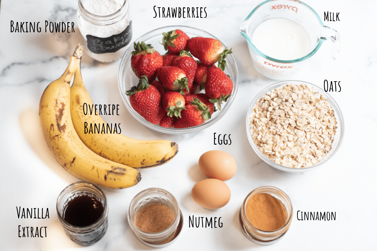 brown bananas, strawberries, oats, spices, vanilla extract, milk, baking soda and eggs on a counter and labeled. 