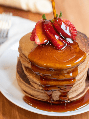 a stack of pancakes with syrup being poured on.