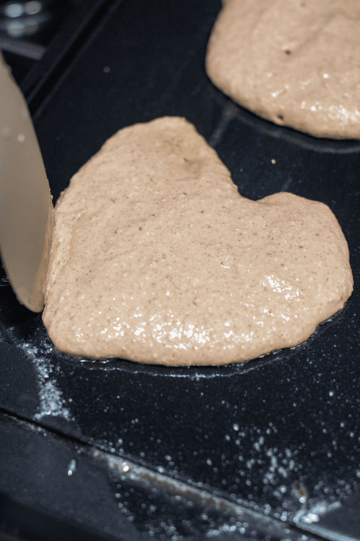 raw pancake batter on a griddle in the shape of a heart.