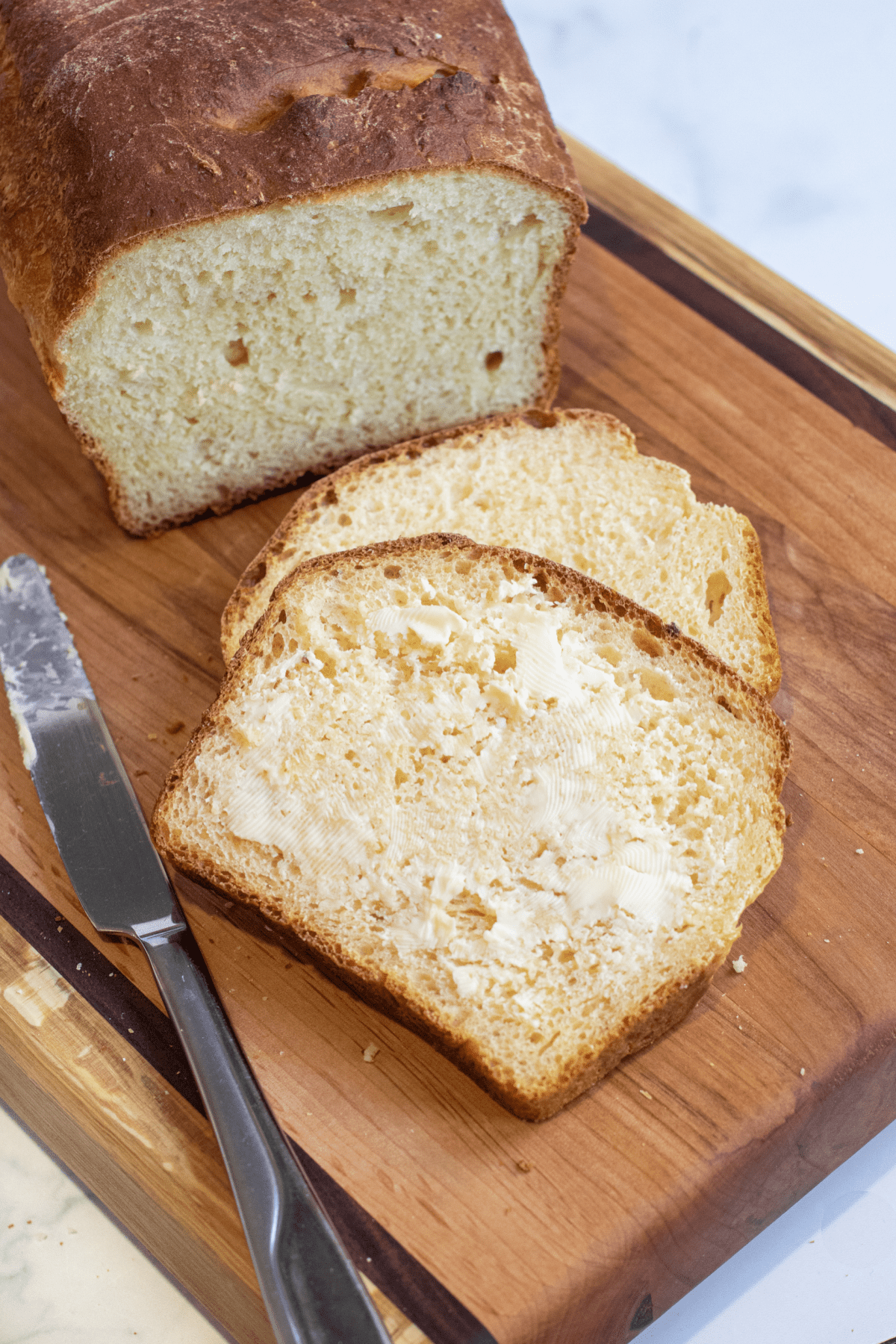 two pieces of sliced bread on a cutting board with one buttered.