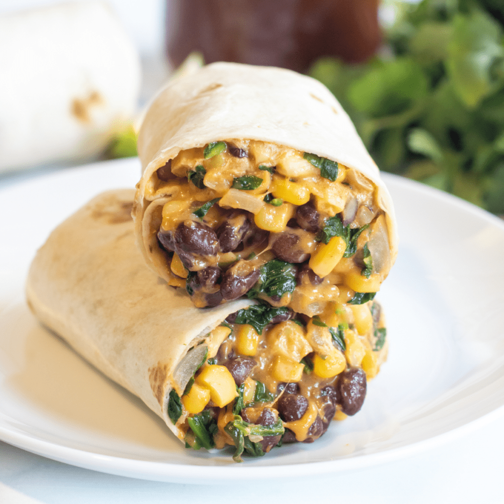 a burrito with beans, corn, and spinach in half on a plate.