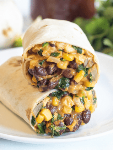 a burrito with beans, corn, and spinach in half on a plate.