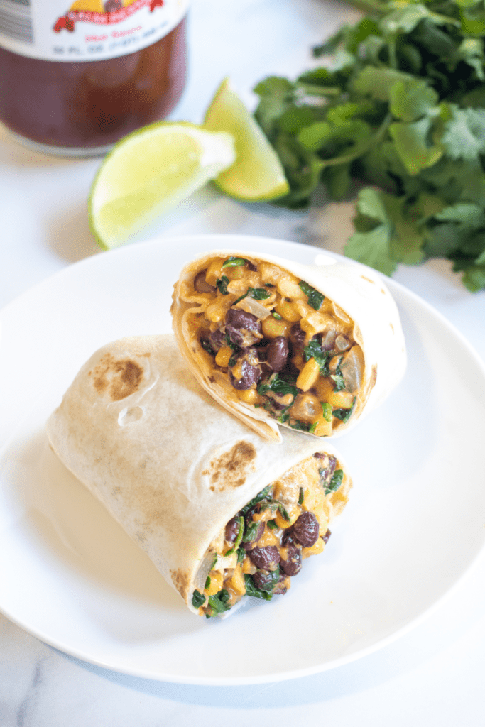 a burrito with beans, corn, and spinach in half on a plate.