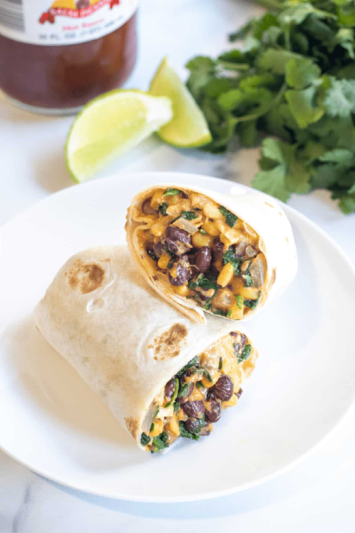 a half of a burrito on a plate with beans, corn, and spinach.