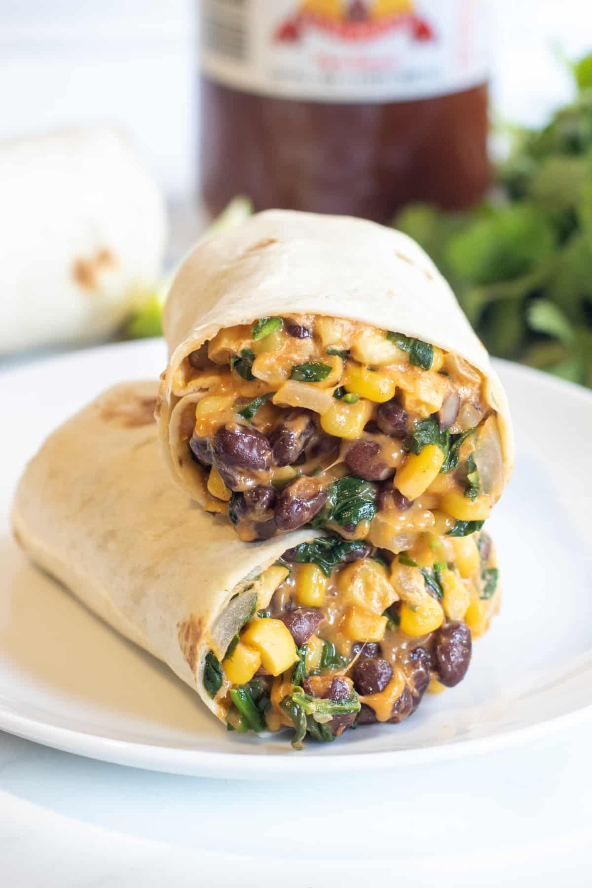 a half of a burrito on a plate with beans, corn, and spinach.