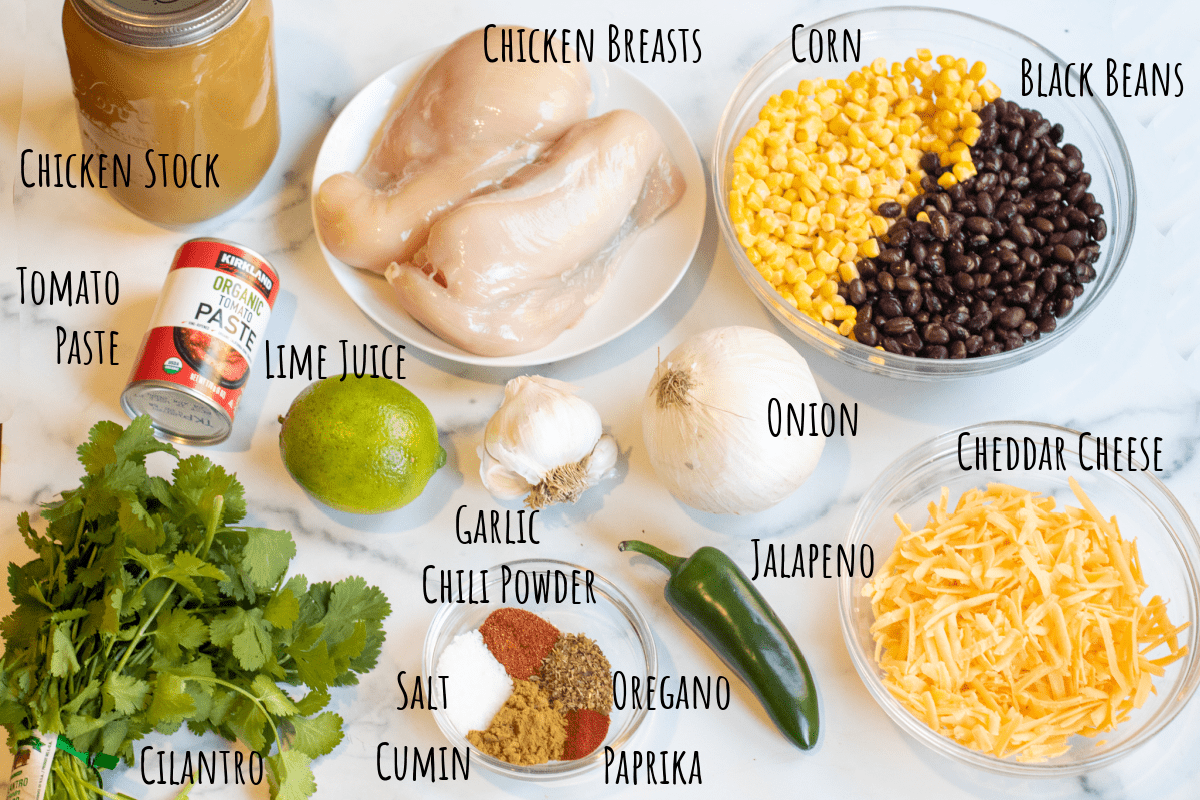 stock, chicken, cheese, corn, black beans, cilantro, lime, spices, onion, garlic, tomato paste, jalapeno on a counter.