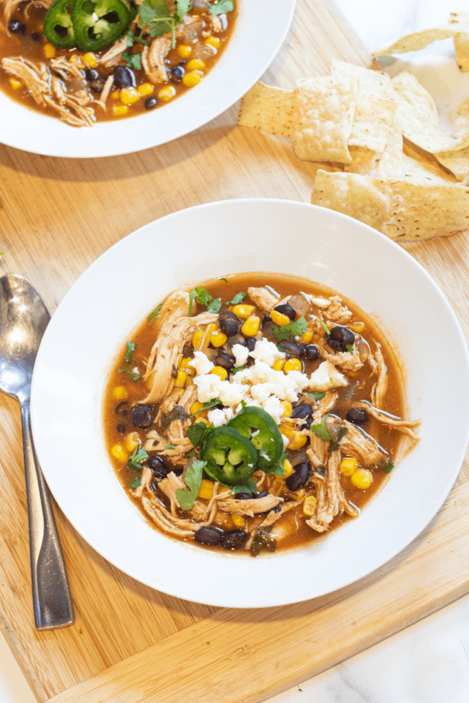 a bowl of chicken enchilada soup with cheese and sliced jalapenos.