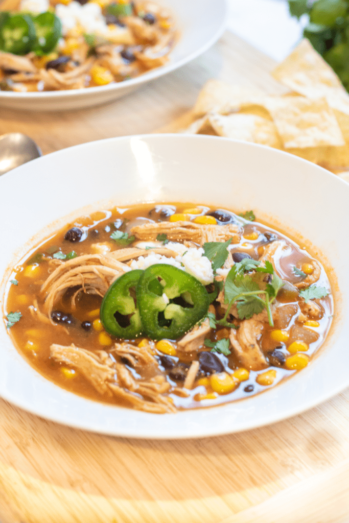 a bowl of chicken enchilada soup with cheese and sliced jalapenos.