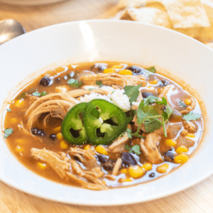 a bowl of chicken enchilada soup with cheese and sliced jalapenos.