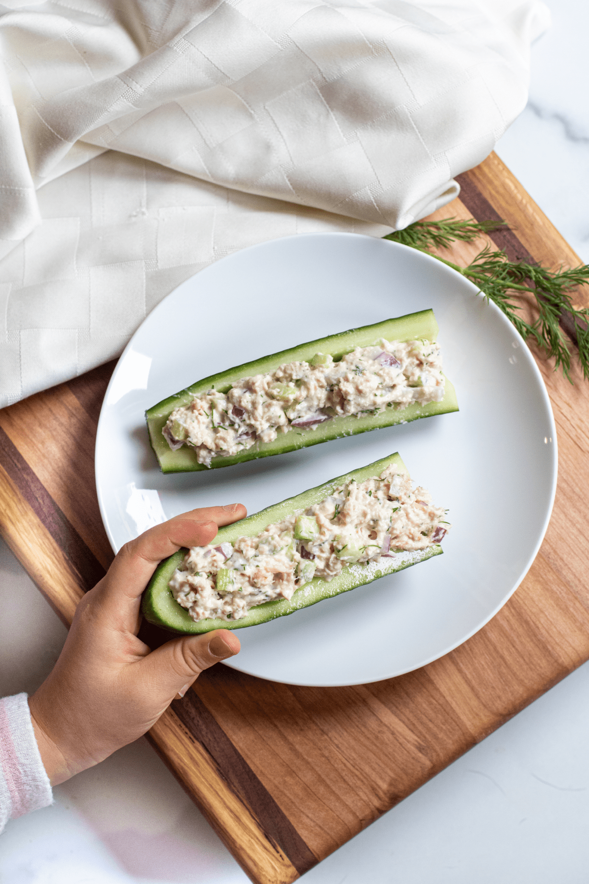 a kids hand holding a cucumber boat with tuna salad.