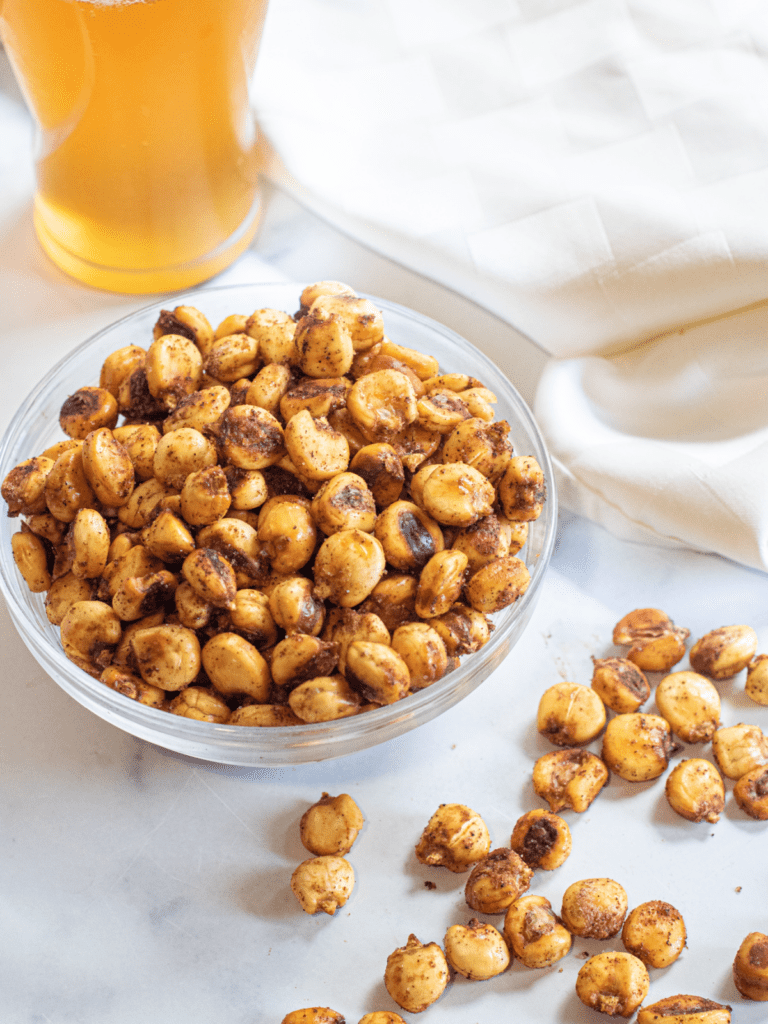 a bowl of corn nuts next to a beer.