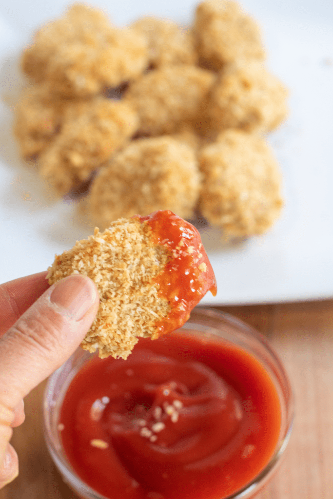 a hand holding up a chicken nugget dunked in ketchup.