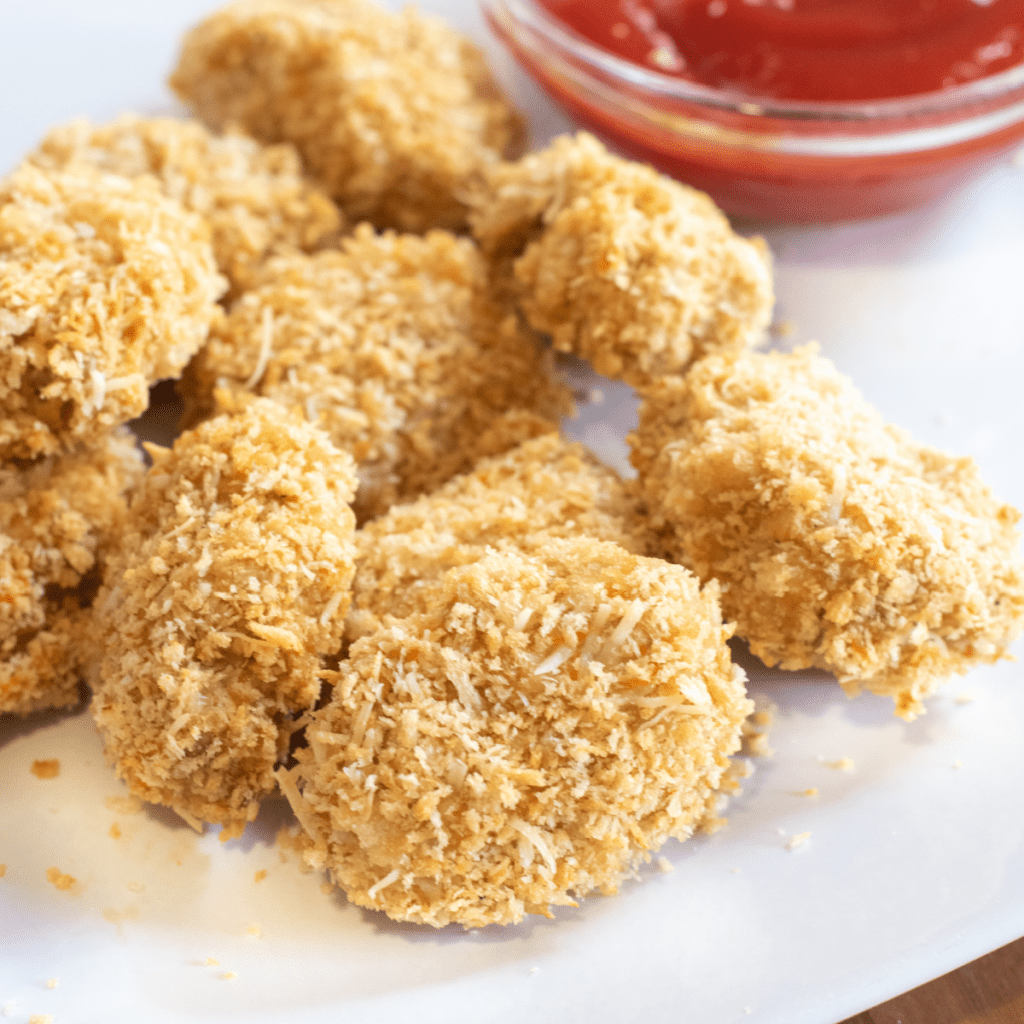 a plate of baked chicken nuggets on a plate next to ketchup.