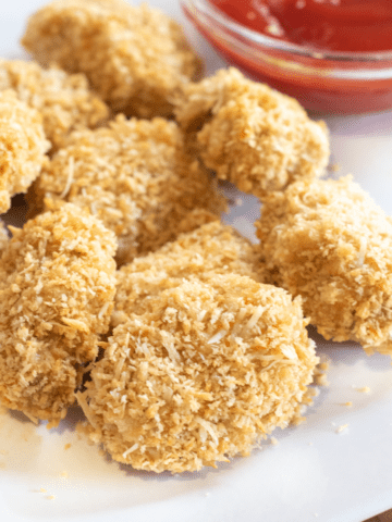 a plate of baked chicken nuggets on a plate next to ketchup.