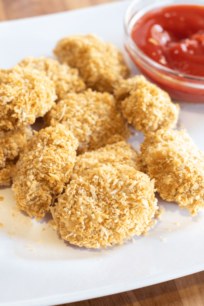 a plate of baked chicken nuggets with a bowl of ketchup.