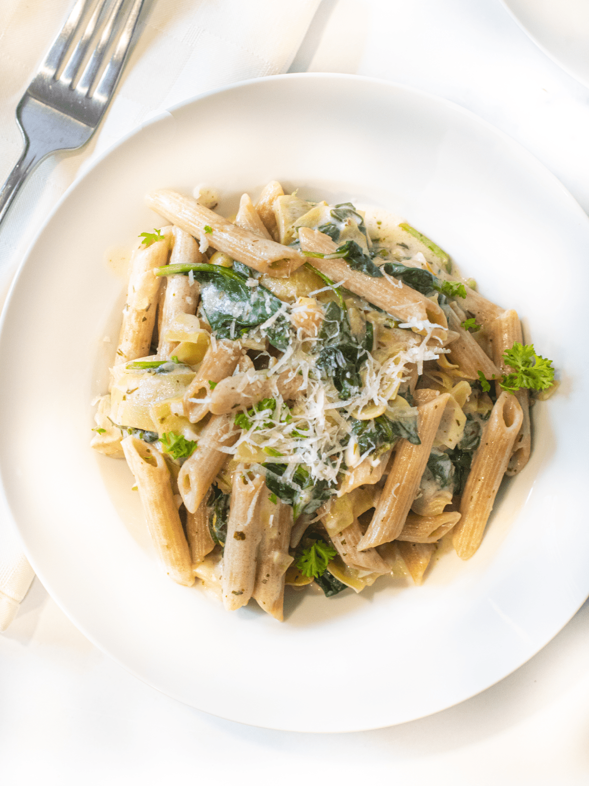 overhead of a plate of pasta with spinach artichokes and cheese.