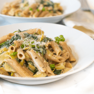 a close up of a bowl of pasta with spinach and artichokes topped with Parmesan cheese.