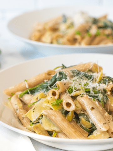 a close up of a bowl of pasta with spinach and artichokes topped with Parmesan cheese.