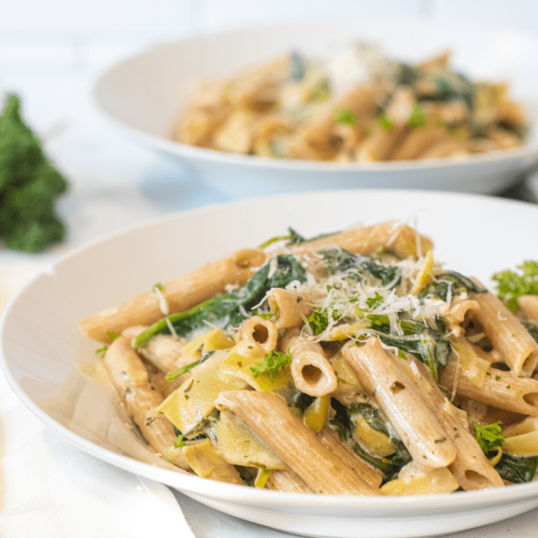 a close up of a bowl of pasta with spinach and artichokes topped with Parmesan cheese.