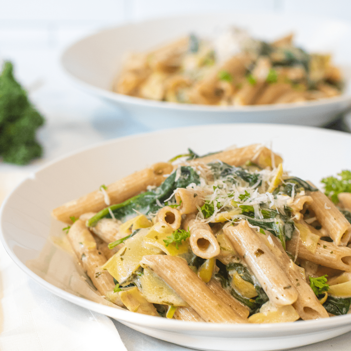 a close up of a bowl of pasta with spinach and artichokes topped with Parmesan cheese.