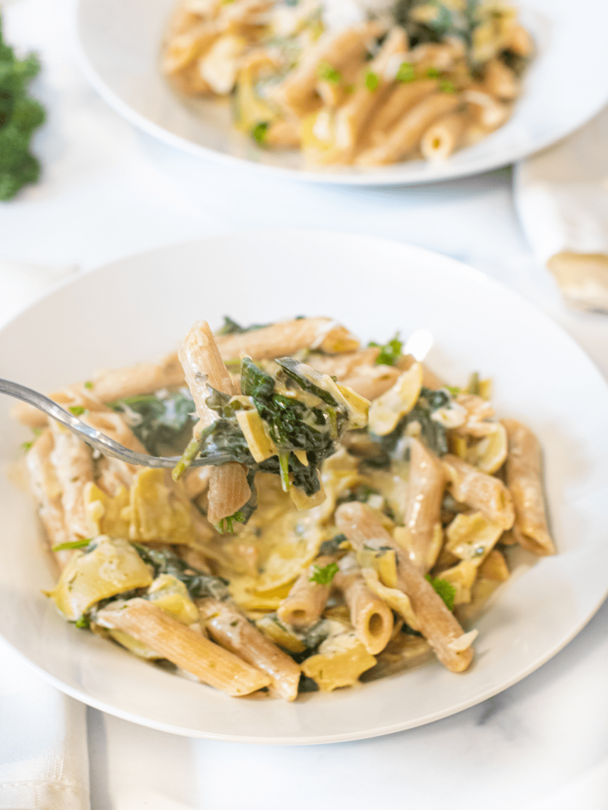 a bowl of spinach artichoke pasta with a forkful being held up.