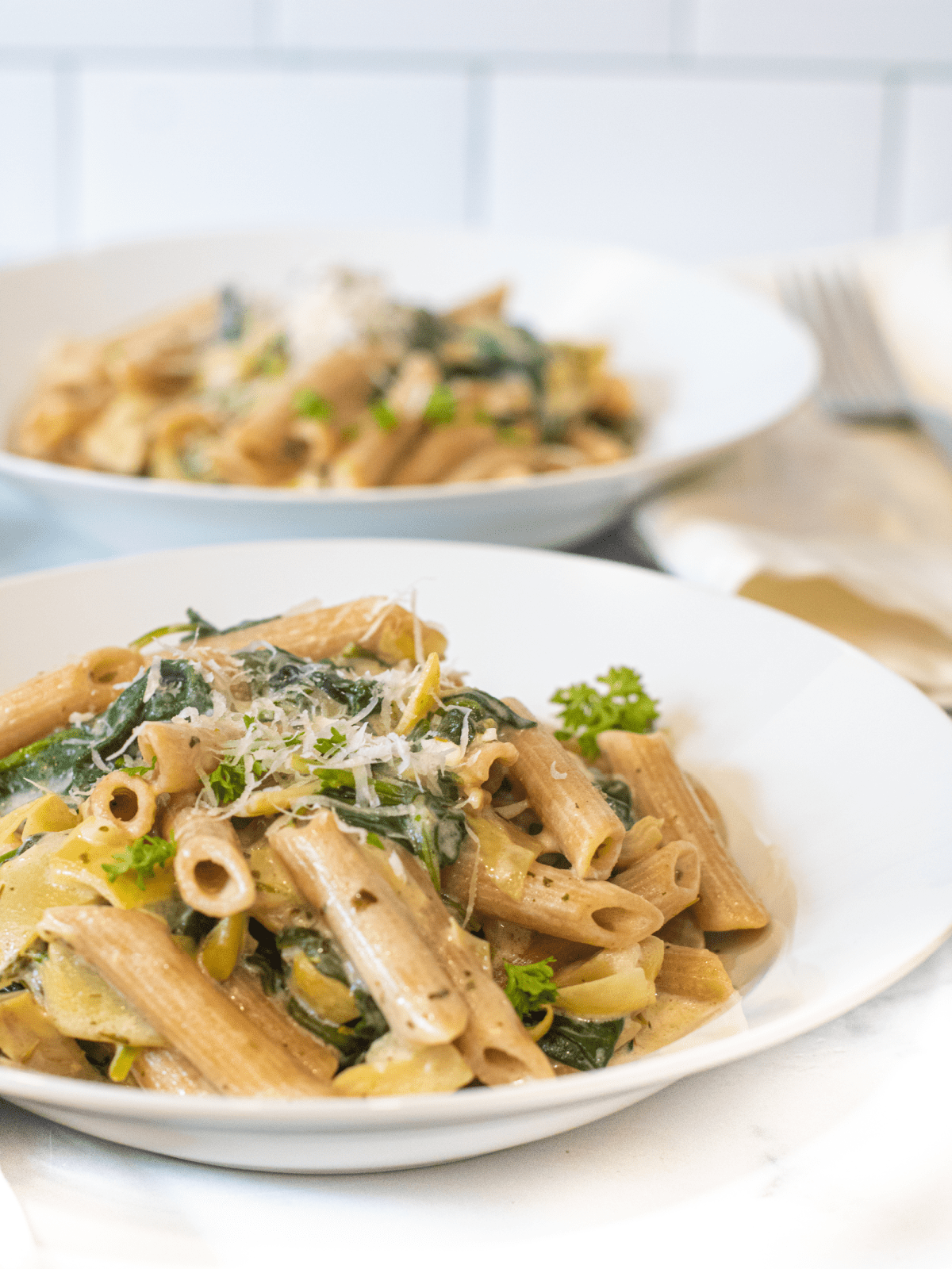 a close up of a bowl of pasta with spinach and artichokes topped with Parmesan cheese.