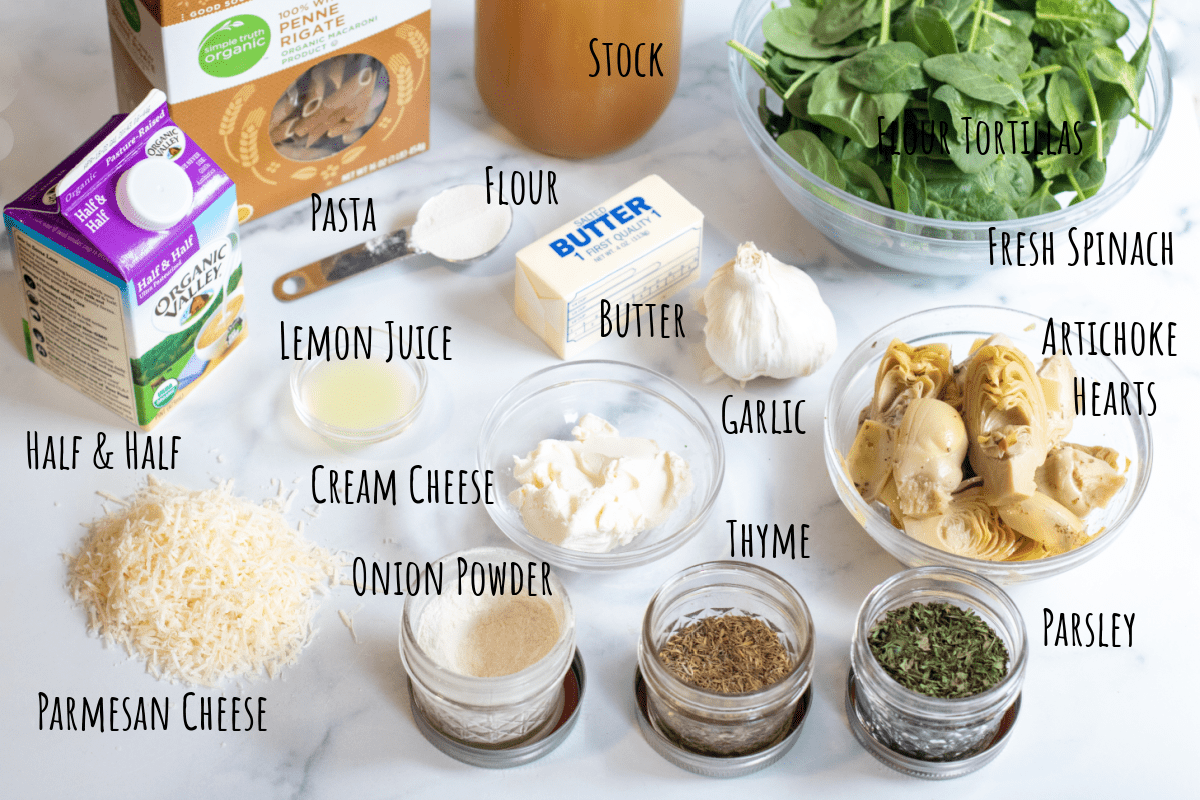 pasta, half and half, stock, butter, spinach, artichokes, cream cheese, spices, parmesan cheese, butter, and garlic on a counter.