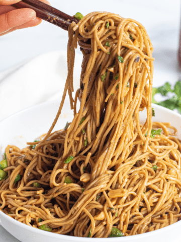 chopsticks holding up peanut noodles over a large bowl of noodles.