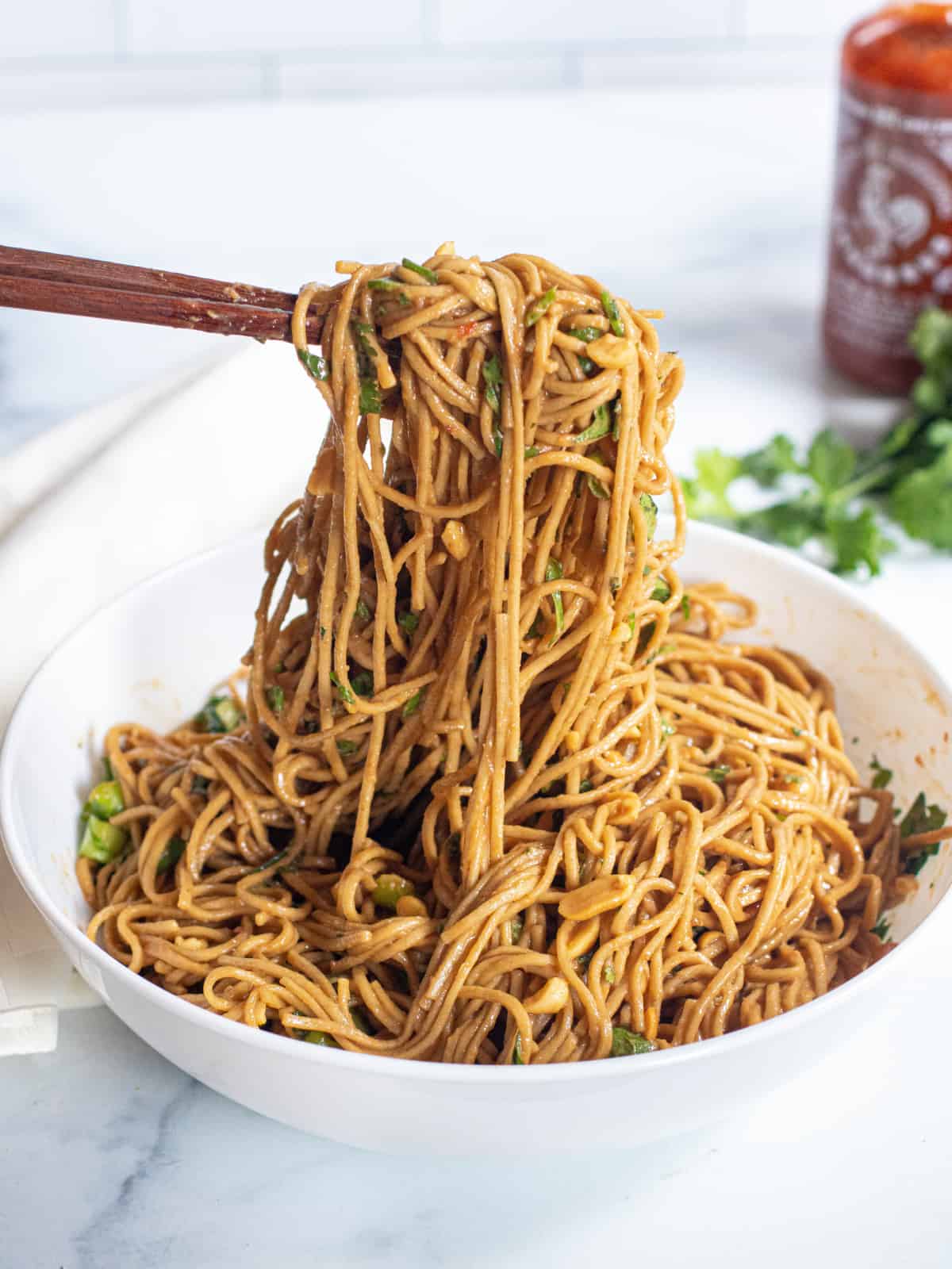 chopsticks holding up peanut noodles over a large bowl of noodles.