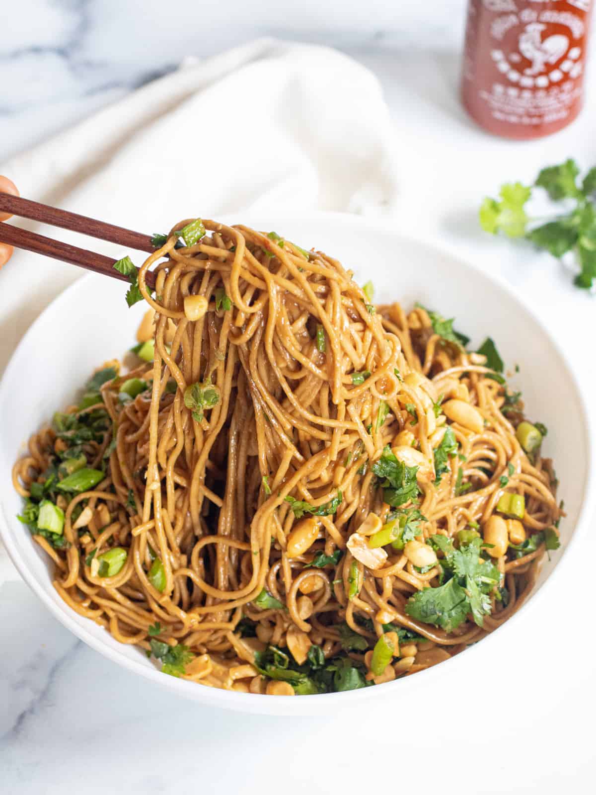 chopsticks holding up peanut noodles over a large bowl of noodles.
