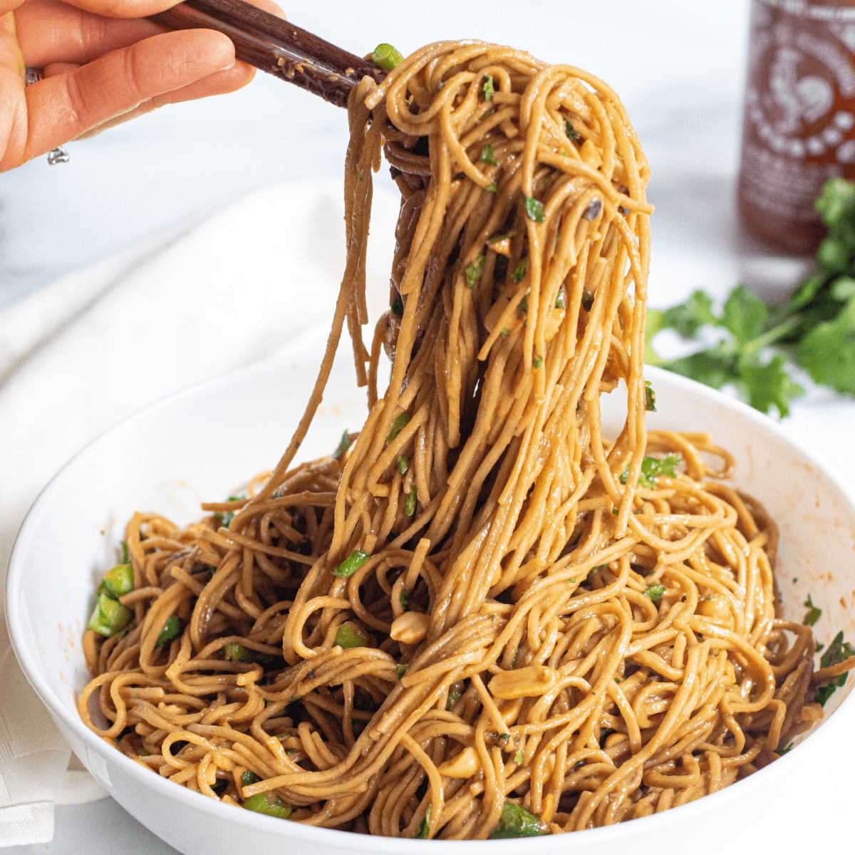 chopsticks holding up peanut noodles over a large bowl of noodles.