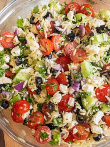 a bowl of orzo with cucumber, tomatoes, olives, feta cheese, and parsley.