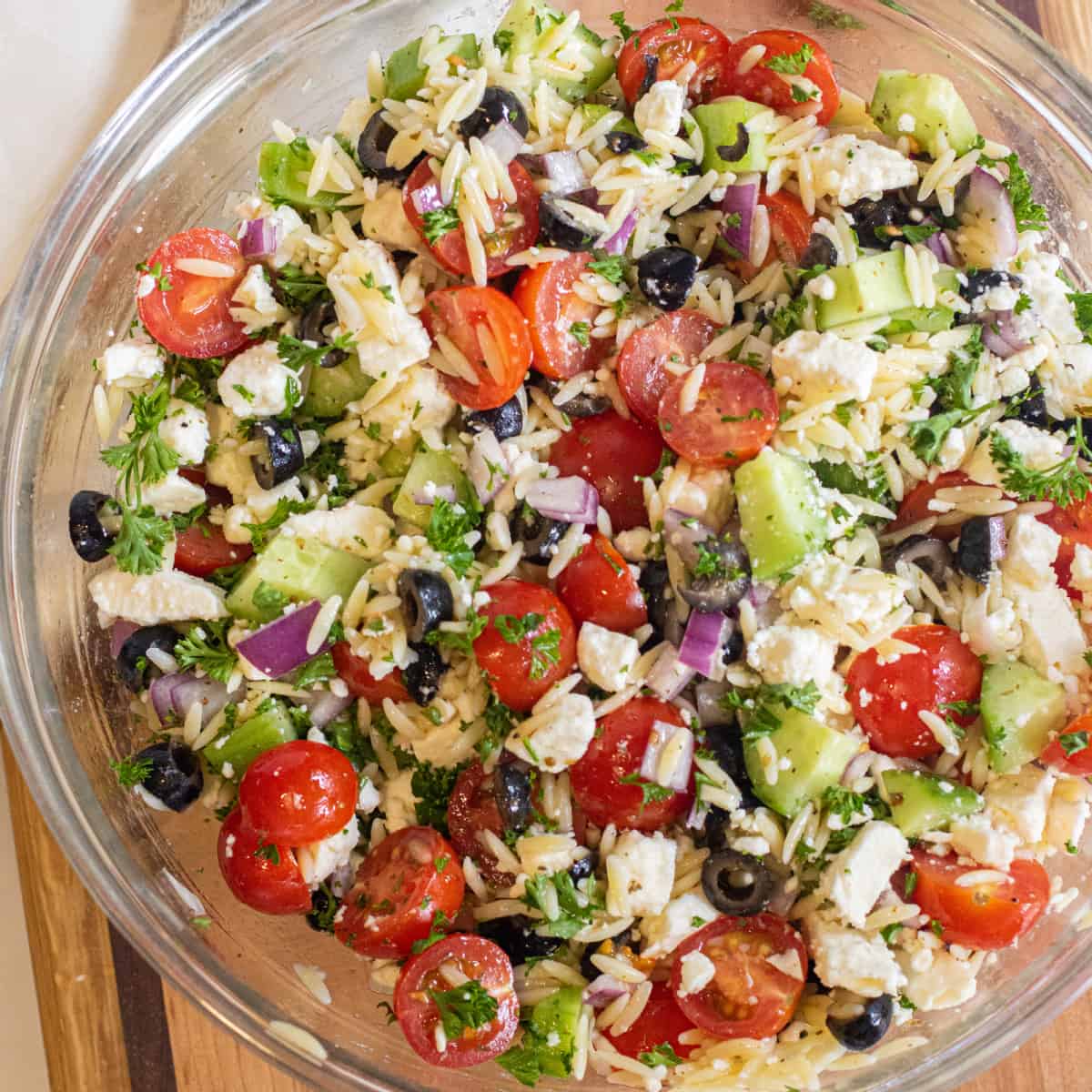 a bowl of orzo with cucumber, tomatoes, olives, feta cheese, and parsley.