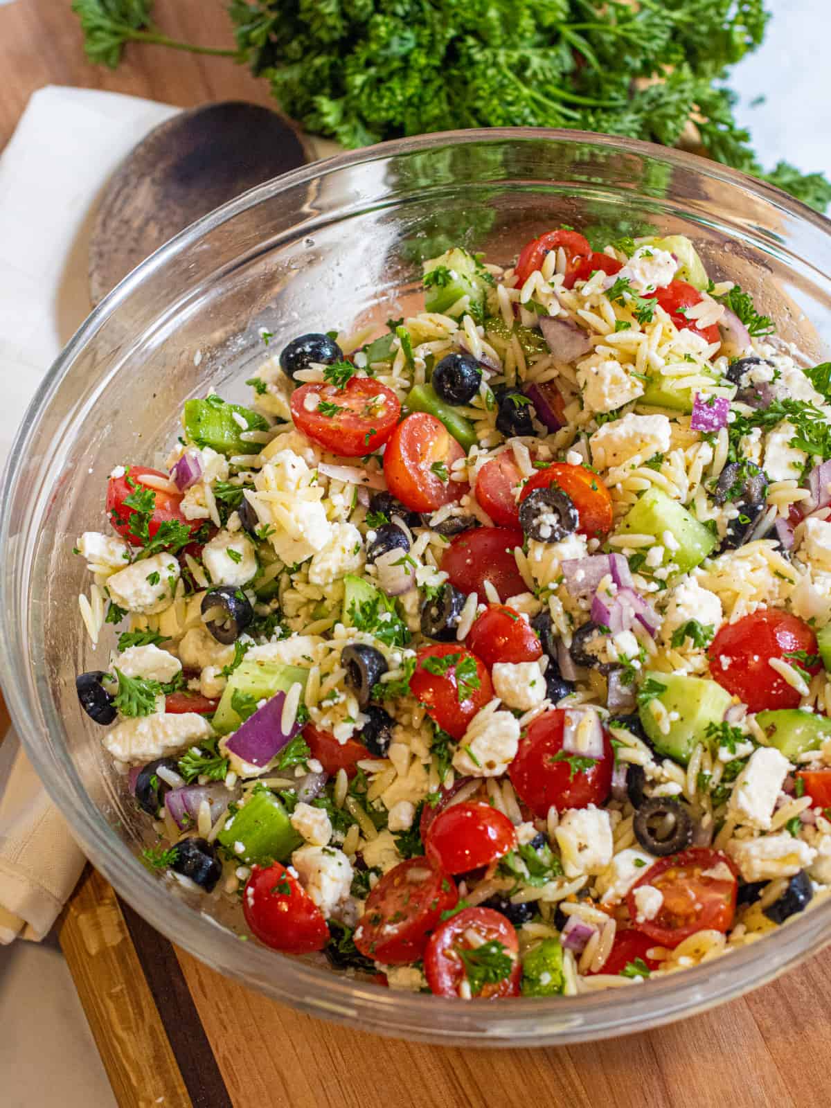 a bowl of orzo with cucumber, tomatoes, olives, feta cheese, and parsley.
