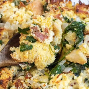 a close up of a spoon with a breakfast strata with spinach and bacon.