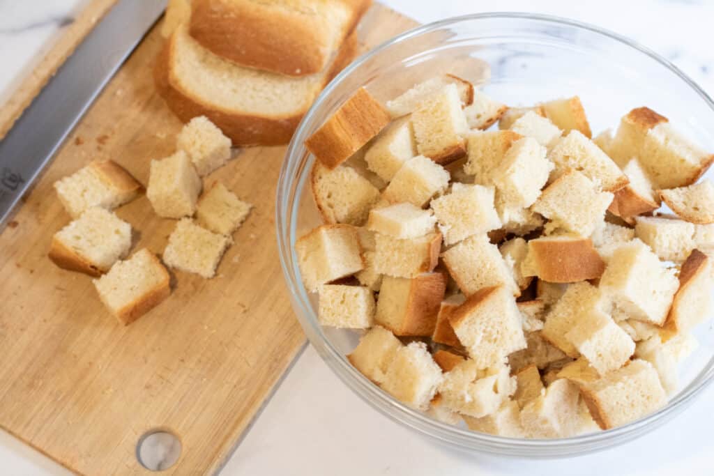sliced bread on a cutting board and cubed in a bowl.
