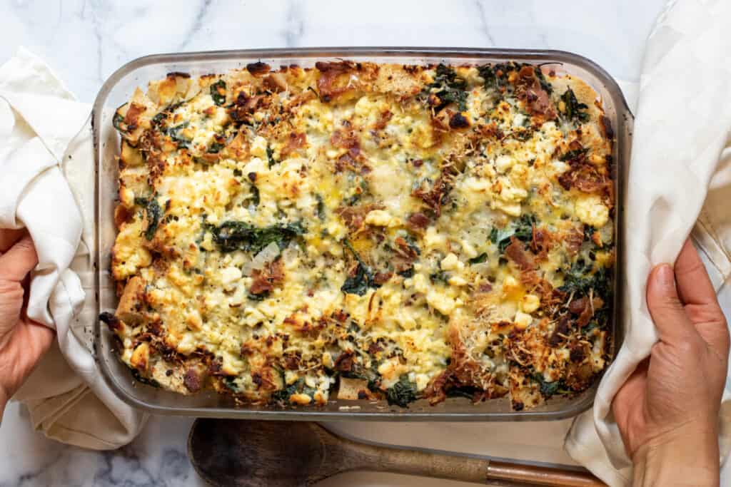 a baking dish with cheese and spinach and bacon strata.