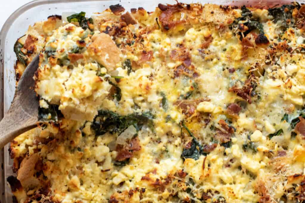 a baking dish with cheese and spinach and bacon strata.