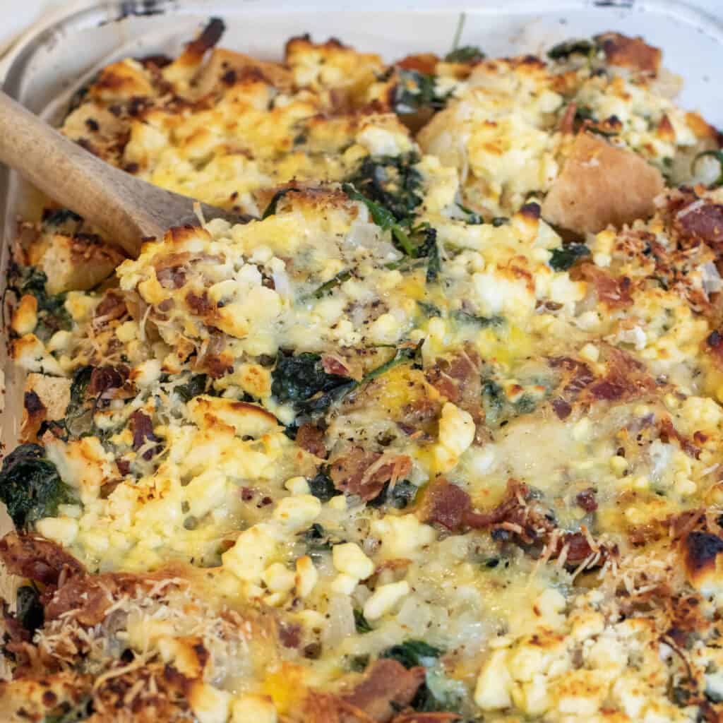 a baking dish with cheese and spinach and bacon strata.